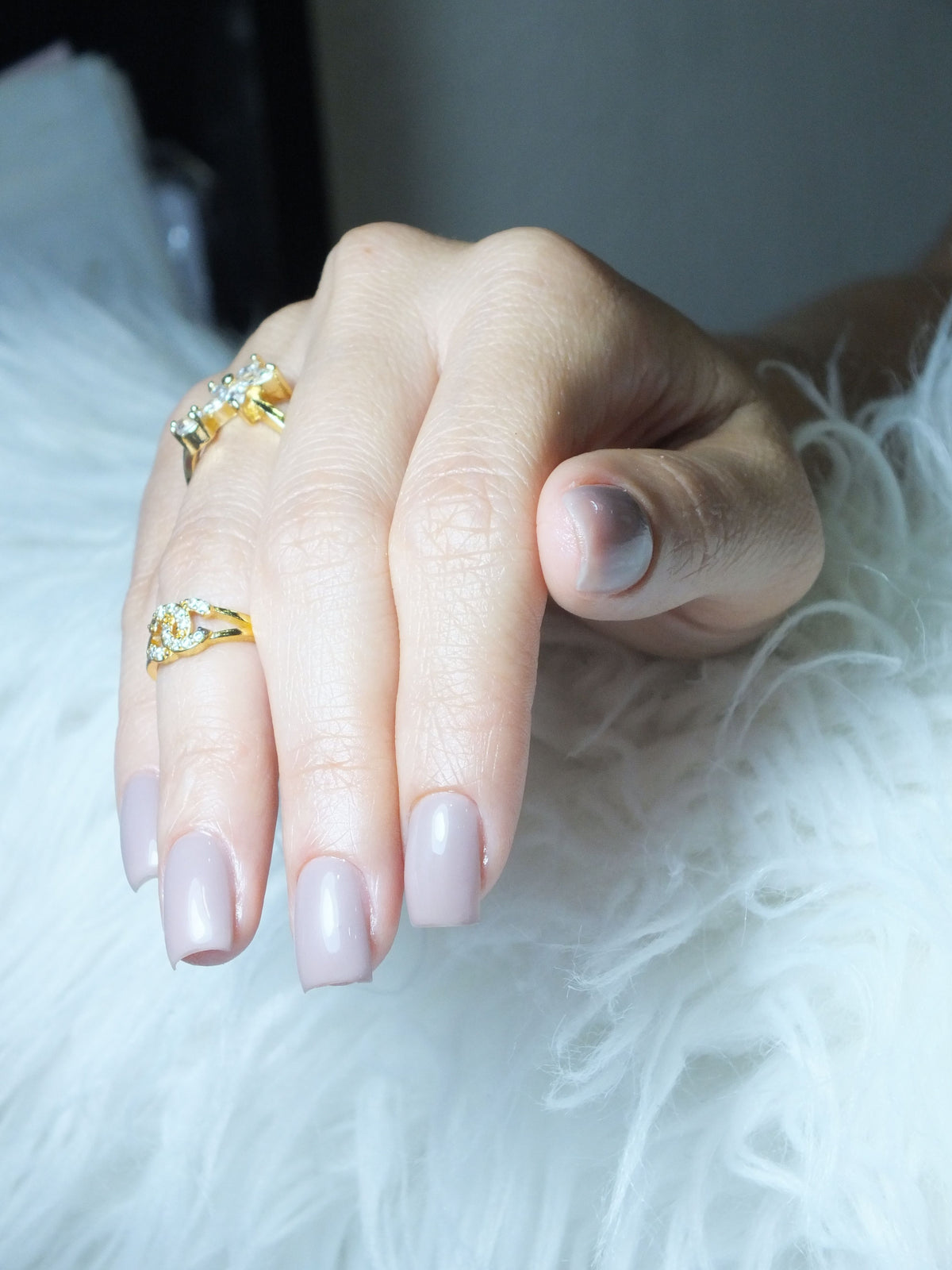 Main manucurée avec bagues dorées sur fond blanc, ongles de qualité longue durée