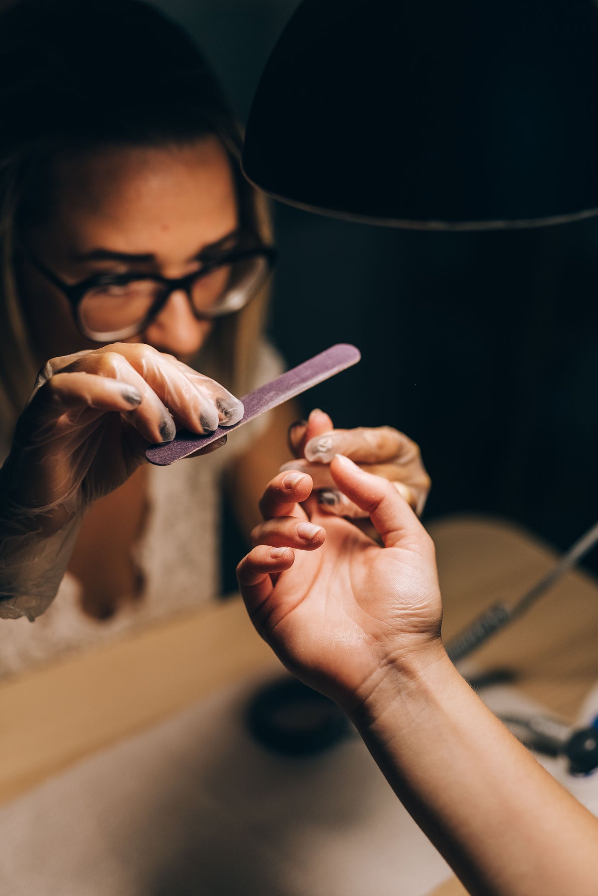 Manucure limant les ongles d'une cliente en institut sous une lumière douce